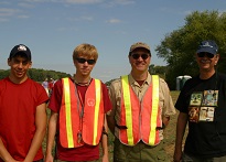 Four men standing posing for a photo, two of them wearing orange safety vests